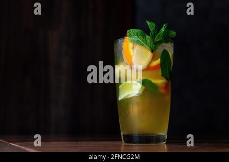Kalte Limonade mit Scheiben aus Zitrone, Orange und Ingwer mit Minzblättern. Kaltes Erfrischungsgetränk oder Getränk mit Eis auf einem Holztisch. Dunkler Hintergrund. Speicherplatz kopieren. Stockfoto