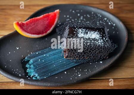 Schokoladendessert mit Grapefruit-Eis auf einem anmutigen Teller. Schickes Dessert, Schokoladenbrownie. Süße Bäckerei und Dessert auf Holzhintergrund. Stockfoto