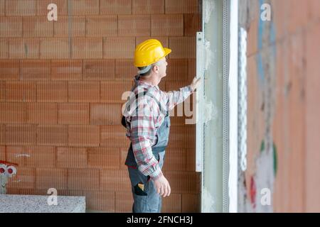 Leitender männlicher Bauarbeiter, der die Wand misst Stockfoto
