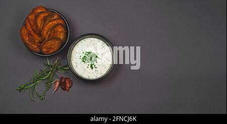Arial Ansicht von knusprig gebackenen Süßkartoffelchips garniert mit Chili, Rosmarin und Thymian und Joghurt Knoblauch Schnittlauch Dip Sauce in schwarzen Schalen Stockfoto