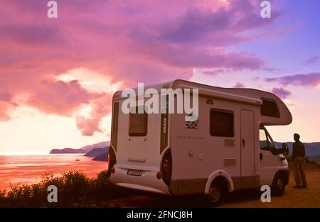 Mann bei seinem Camper bei Sonnenuntergang über der Insel Elba * Reisemobil an stimmungsvoller Aussicht auf die Südküste der Insel Elba . Stockfoto