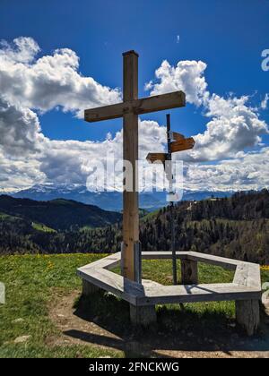 Gipfelkreuz auf dem schönen Grashügel huettchopf im zürcher oberland schweiz. Schöne Sicht auf die Berge. Bank Stockfoto