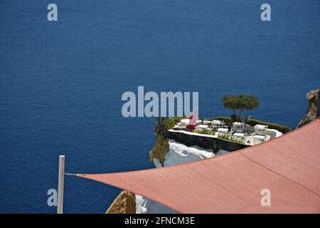 Malerische Landschaft mit einer exklusiven Veranda mit Blick auf die Ägäis, die durch ein Sonnenschirmsegel auf der Insel Santorini, Kykladen, Griechenland, gesehen wird. Stockfoto