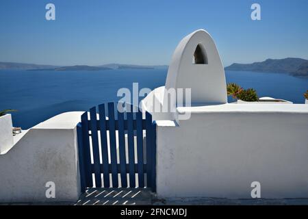 Traditionelle lehmhausfassade mit einer weiß getünchten Wand, einer blauen hölzernen Zauntür und einem kykladischen Kamin auf Santorini, Griechenland. Stockfoto