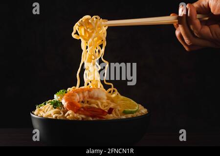 Hand mit Stäbchen pickup instant Nudeln mit auf schwarzem Hintergrund isoliert raucht. Stockfoto