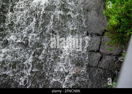 Wasser fließt über schwarze Steine eines Wehrs Stockfoto