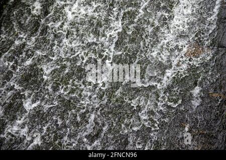 Wasser fließt über schwarze Steine eines Wehrs Stockfoto