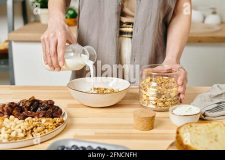 Eine Frau gießt Milch in die Schüssel mit Maisflocken durch Küchentisch Stockfoto