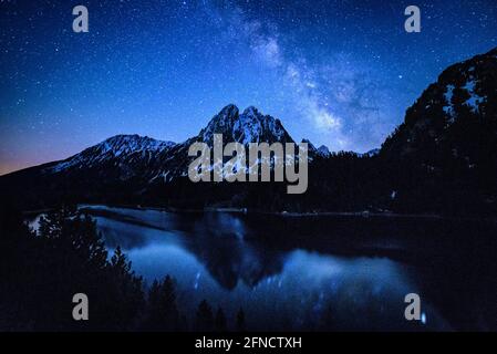 Encantats Zwillingsgipfel vom Estany de Sant Maurici See aus gesehen in einer Frühlingsnacht mit der Milchstraße über dem Berg (Aiguestortes, Katalonien, Spanien) Stockfoto