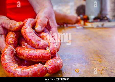 Blick auf Stapel frischer, roter, handgefertigter, einheimischer Würstchen in Metzgerhand in der Außenküche. Stockfoto