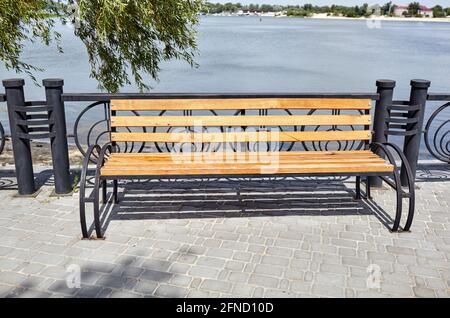 Böschung mit Bank mit Blick auf das Meer. Parken Sie die Holzbank auf dem gepflasterten Bürgersteig Stockfoto