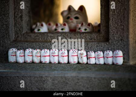 Ein weicher Fokus einer Reihe winkender Katzenskulpturen Auf einer Betonoberfläche Stockfoto