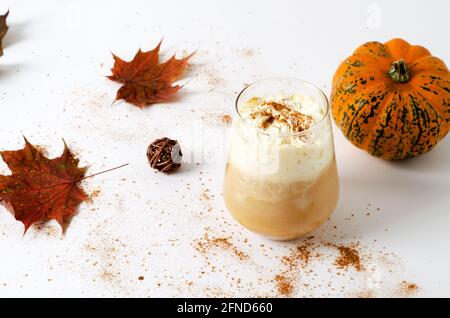 Würziger Kürbis-Latte in einem Glas mit Creme und Zimt. Konzept eines herbstlichen warmen Getränks mit Kürbissen und Herbstblättern auf weißem Hintergrund mit Copy Spa Stockfoto