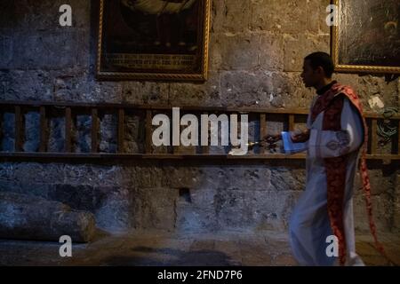 Ein Priester, der mit einem Weihrauchbrenner auf einem halbdunklen Flur in der Kirche des Heiligen Grabes von Jerusalem geht. Stockfoto