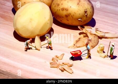 Konzeptuelles Bild von Miniaturfiguren, die Kartoffeln auf einem schälen Hölzerne Chooping Board Stockfoto