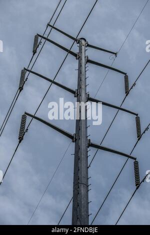 Blick nach oben auf den oberen Teil eines Turms, dass Stromversorgung über Kabel, das mit einem an die Isolatoren angeschlossen ist Bewölktes Himmel im Hintergrund Stockfoto