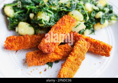 Gebratene Fischstäbchen, knusprig und golden serviert mit Schweizer Mangold und gekochten Kartoffeln Stockfoto