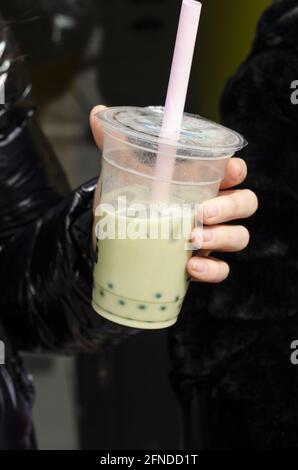 Eine Frau, die eine Plastikschale mit Milchtee hält Mit einem Strohhalm Stockfoto