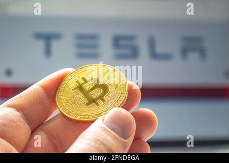 Calgary, Alberta, Kanada. 14.Mai 2021. Eine Person, die eine Bitcoin mit dem Tesla-Logo auf dem Hintergrund hält Stockfoto