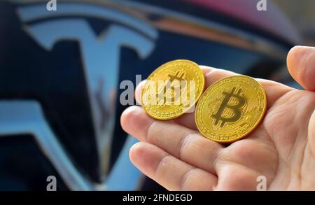 Calgary, Alberta, Kanada. 14.Mai 2021. Eine Person, die ein paar Bitcoins mit dem Tesla-Auto auf dem Hintergrund hält Stockfoto