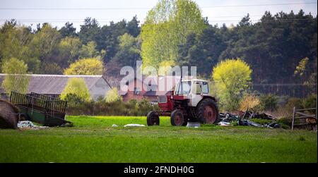 Ein alter, verlassene Traktor, der vor einem Hintergrund entfernter Bauernhöfe steht. Unscharfer Hintergrund. Das Foto wurde bei natürlichem Tageslicht aufgenommen. Stockfoto