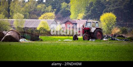 Ein alter, verlassene Traktor, der vor einem Hintergrund entfernter Bauernhöfe steht. Unscharfer Hintergrund. Das Foto wurde bei natürlichem Tageslicht aufgenommen. Stockfoto