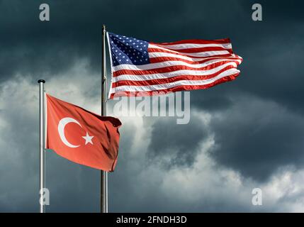 Staatsflaggen der USA und der Türkei flattern vor einem dunklen, stürmischen Himmel, symbolisches Bild für schwierige politische Beziehungen zwischen den USA und der Türkei Stockfoto