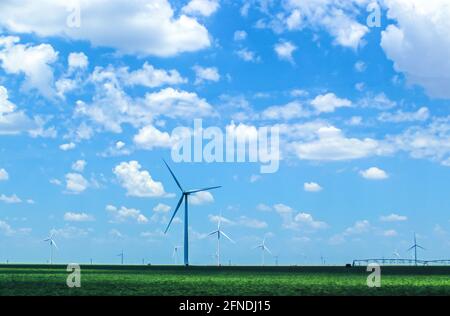 Windturbinen im landwirtschaftlichen Feld auf Plains unter schönem Blau wolkiger Himmel mit Bewässerungsanlagen in der Ferne - selektiver Fokus Stockfoto