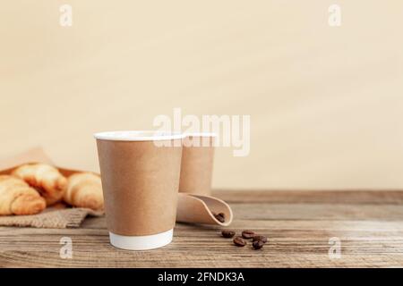 Zwei Pappbecher Kaffee, Croissants, Kaffeebohnen und Löffel am Holztisch Stockfoto