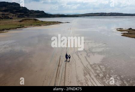 Zwei Wanderer folgen Reifenspuren im Sand, die zur Gezeiteninsel Oronsay, der Strand Isle of Colonsay, Schottland, Großbritannien, führen Stockfoto