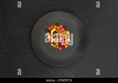 Bunte Süßigkeiten auf dem schwarzen Teller isoliert auf dunklem Hintergrund Stockfoto
