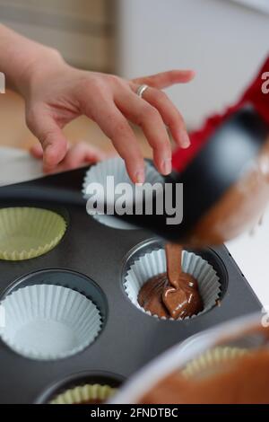 Asiatische philippinische Frau, die ihrem Kind zu Hause in Ottawa, Ontario, Kanada, Schokoladensauce in Cupcakes gießt Stockfoto