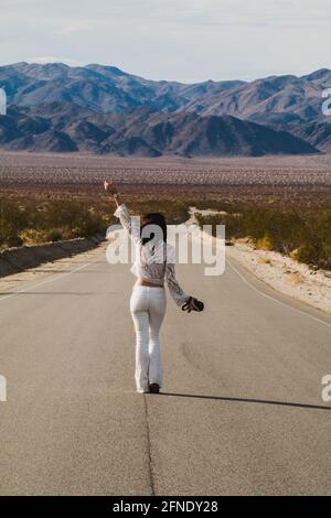 Eine junge Frau, in Weiß gekleidet, die eine trostlose Wüste hinunterläuft Straße in der Mojave-Wüste Stockfoto