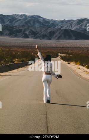 Eine junge Frau, in Weiß gekleidet, die eine trostlose Wüste hinunterläuft Straße in der Mojave-Wüste Stockfoto