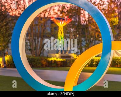 tokio, japan - 10 2021. Mai: Nahaufnahme eines der Ringe des Olympic Rings-Denkmals, das in der Abenddämmerung mit dem beleuchteten olympischen Kessel von Nagano O beleuchtet wird Stockfoto