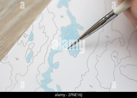 Eine mans Hand hält einen Pinsel und zeichnet ein Bild durch Zahlen. Zeichnen auf Leinwand. Nummerierte Farbdosen. Kreatives Hobby. Malen für Anfänger.Nahaufnahme, sele Stockfoto