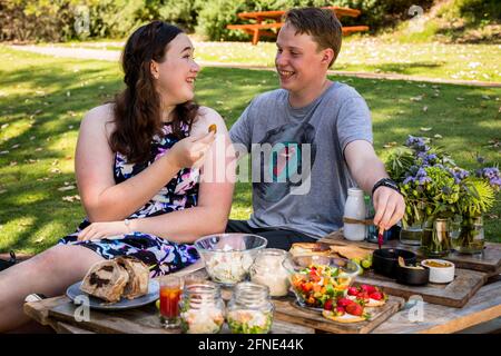 Junges Paar lacht und genießt Gourmet-Picknick Stockfoto