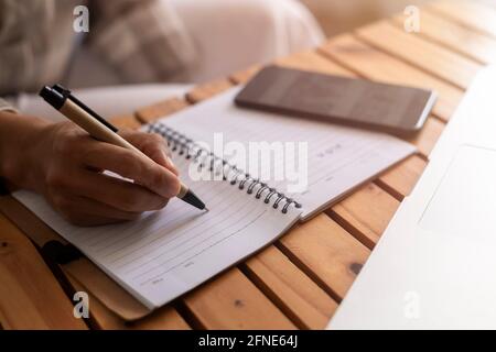 Nahaufnahme junge Geschäftsfrau Hände mit Stift Schreiben Notizen auf Papier. Weibliche Führungskraft sitzt am Tisch im Home Office. Die Hände der Frau schreiben spiralförmig Stockfoto