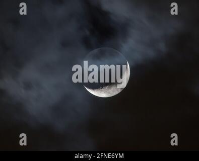 Wolken, die über einem Halbmond vorbeiziehen, erzeugen eine geheimnisvolle Szene am Nachthimmel. Stockfoto