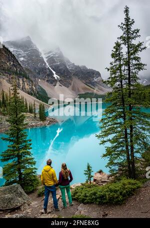 Pärchen blicken über den See, Wolken hängen zwischen Berggipfeln, Spiegelung im türkisfarbenen Gletschersee, Moraine Lake, Valley of the Ten Peaks, Rocky Stockfoto