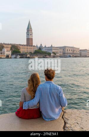 Das junge Paar sitzt am Meer und genießt den Blick auf den Markusplatz mit dem Campanile di San Marco, Venedig, Venetien, Italien Stockfoto