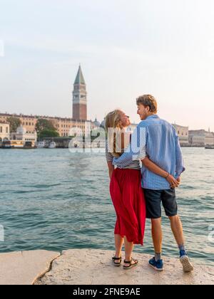 Das verliebte junge Paar steht am Meer und genießt den Blick auf den Markusplatz mit dem Campanile di San Marco, Venedig, Venetien, Italien Stockfoto