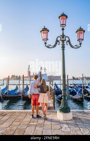 Junges Paar vor einem Steg, venezianische Gondeln, Blick auf die Kirche San Giorgio Maggiore, Venedig, Venetien, Italien Stockfoto