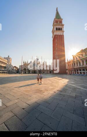 Zwei Touristen schlendern einsam durch den Markusplatz, die Sonne scheint auf dem Markusplatz mit Campanile di San Marco, Venedig, Venetien, Italien Stockfoto