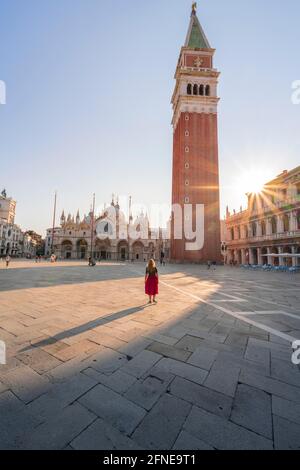 Junge Frau, Tourist mit rotem Kleid am Markusplatz, Sonne scheint auf dem Markusplatz mit Campanile di San Marco, Venedig, Venetien, Italien Stockfoto