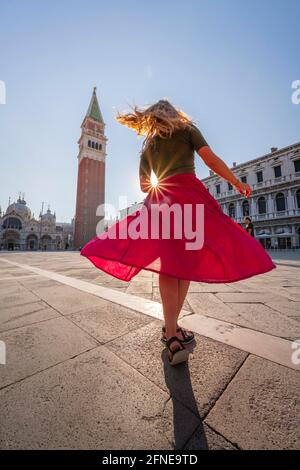 Junge Frau, Tourist mit rotem Kleid am Markusplatz, Sonne scheint auf dem Markusplatz mit Campanile di San Marco, Venedig, Venetien, Italien Stockfoto