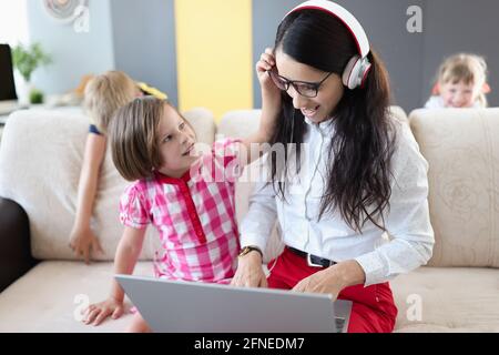 Kleine Kinder hindern ihre Mutter daran, an Laptops zu arbeiten Zu Hause Stockfoto