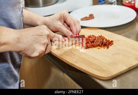 Frau schneidet sonnengetrocknete Tomaten auf Holzbrett, um sonnengetrocknet zu werden Tomatenmuffins Stockfoto