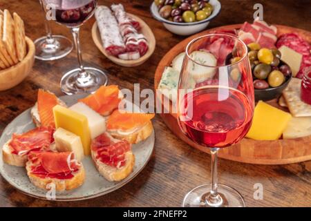 Ein Glas Roséwein mit Sandwiches und einer Käse- und Wurstplatte. Italienische Antipasti oder spanische Tapas. Elegante Gourmet-Vorspeisen Stockfoto