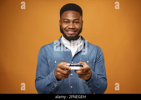Junger afroamerikanischer Mann mit Joystick beim Spielen von Videospielen, gelber Hintergrund Stockfoto